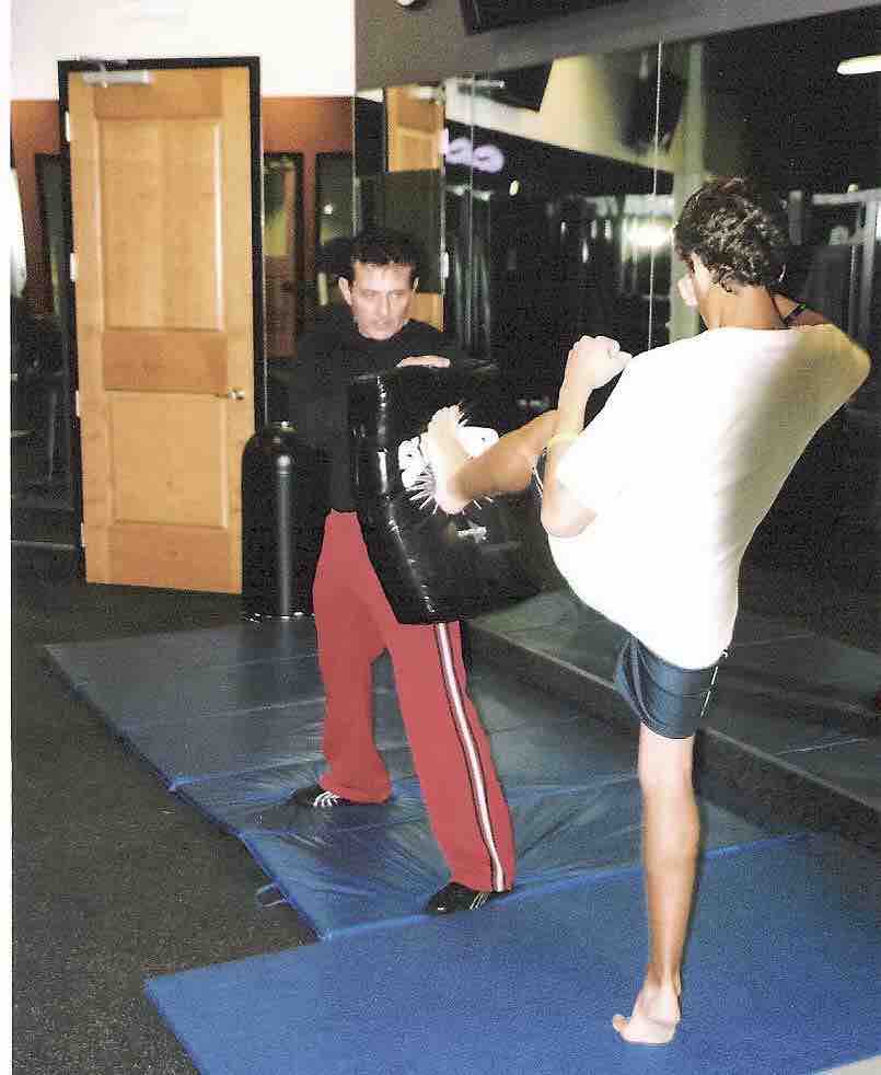 Image of a kickboxing trainer holding a kick sheild for a client performing a roundhouse kick