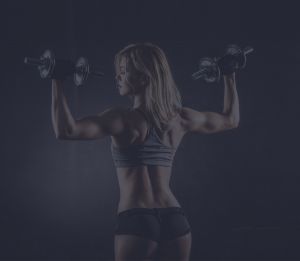Fitness girl lifting two dumbbells in overhead press starting position