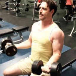 personal trainers client performing a bicep curl with dumbbells in seated position