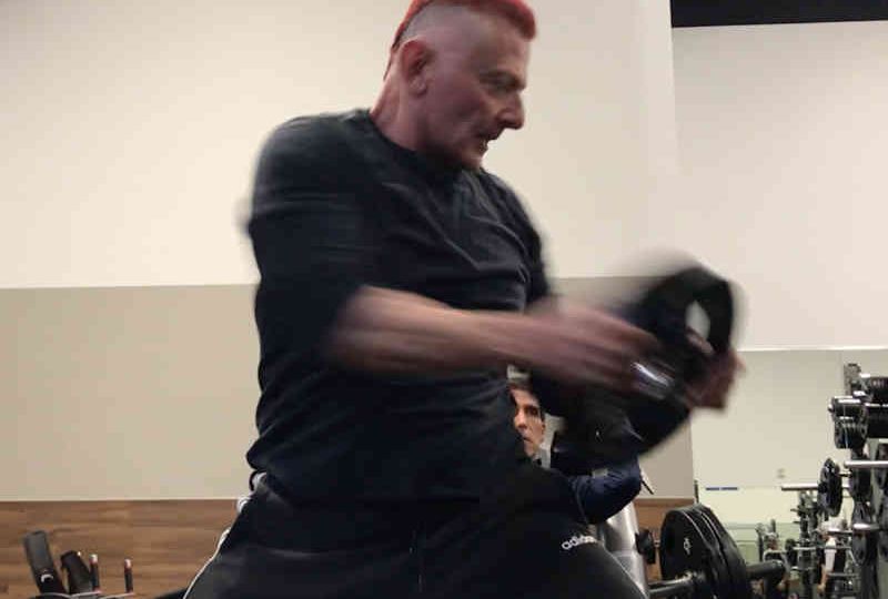 65 year old personal trainer swings a weight plate around his body and head