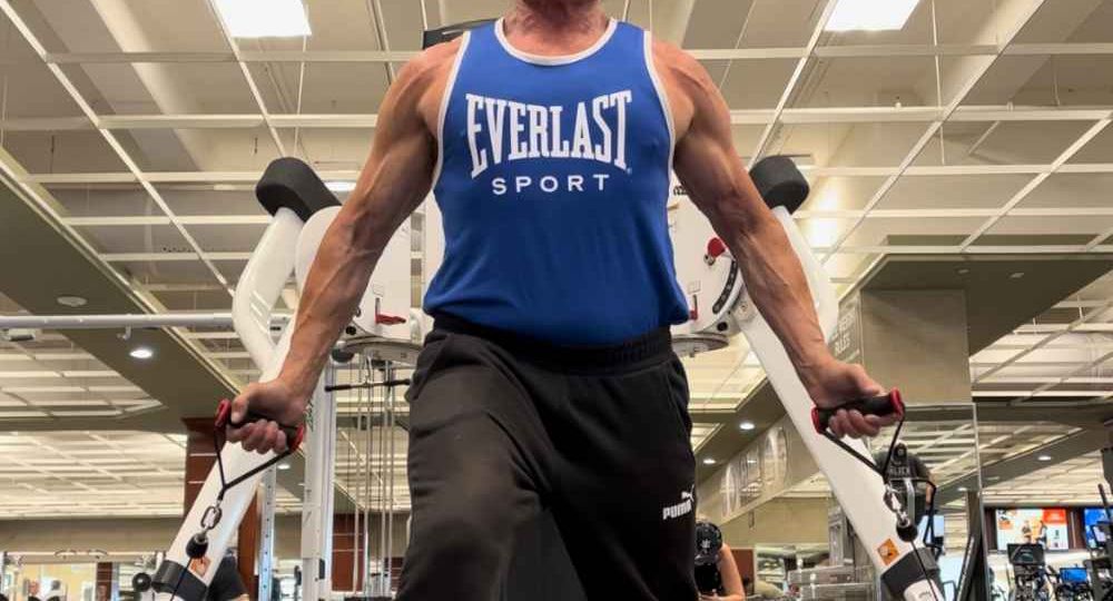 fitness expert holding a cable in each hand palms facing forward to raise cables in front for a chest and shoulder exercise